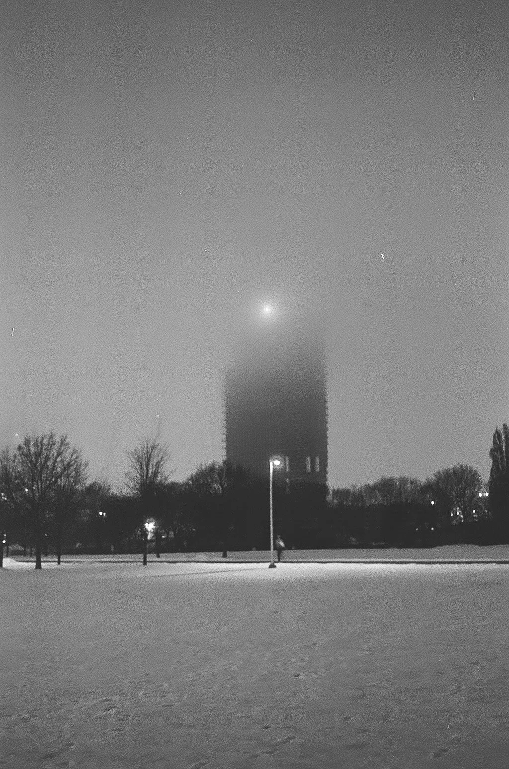 A black and white photo of a building, the top disappearing in the fog.