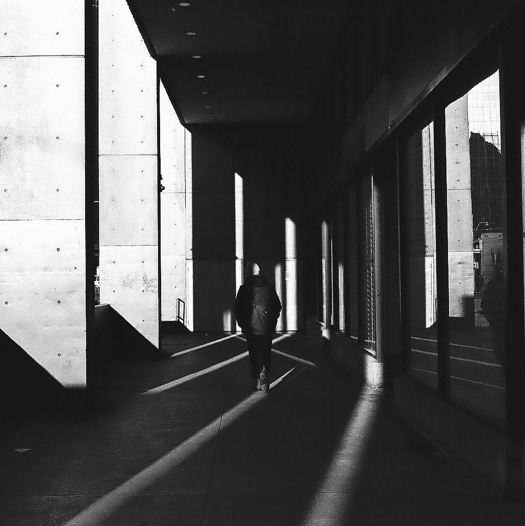 A black and white photo of a person waking in light and shadows.